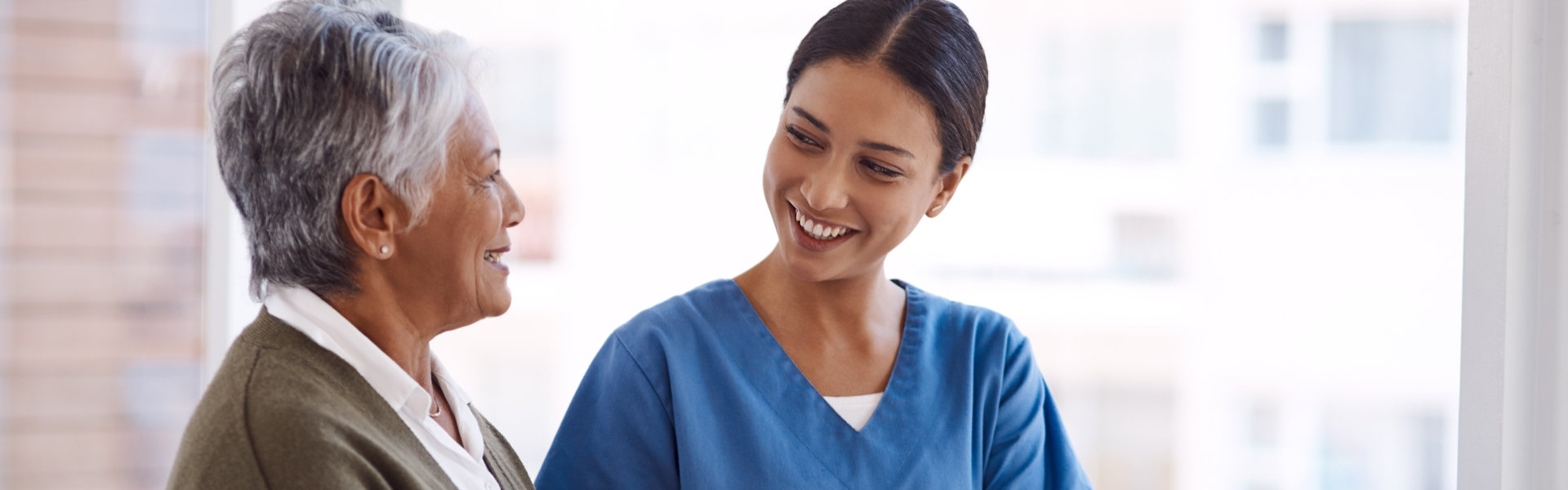 A smiling caregiver and an elderly woman share a warm, engaged conversation.